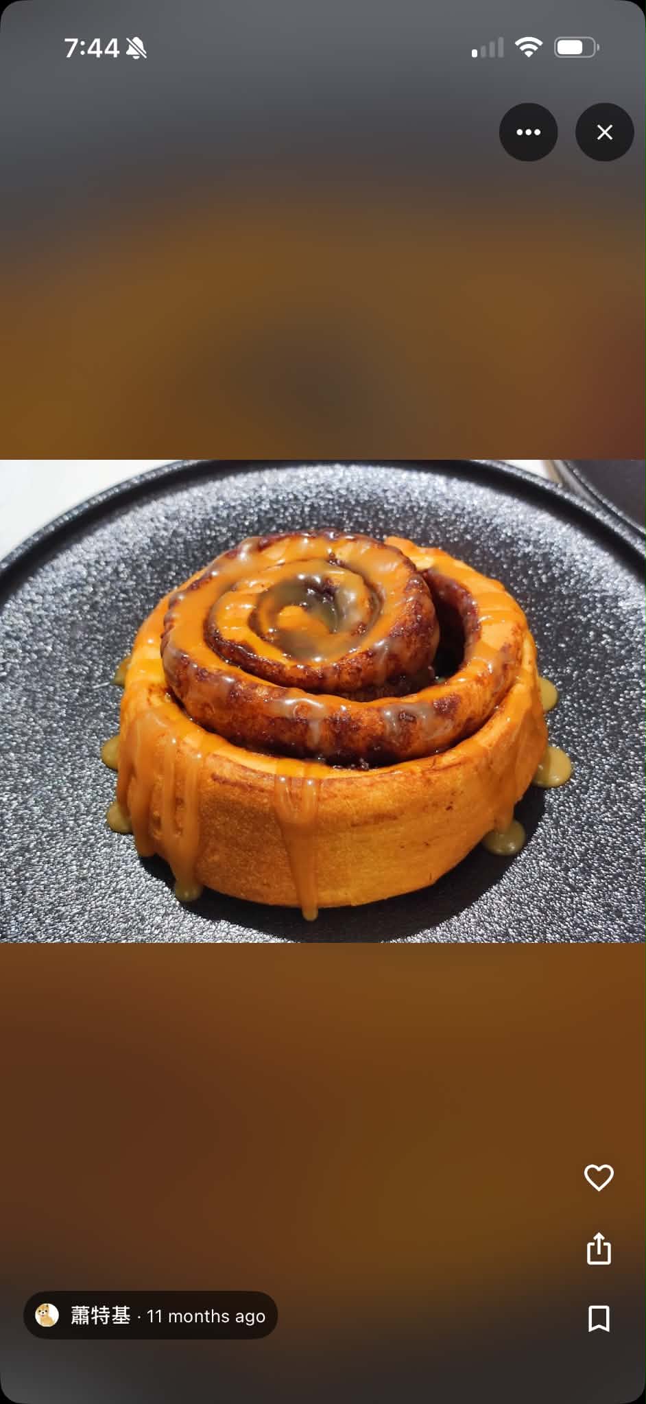 Blurry phone photo of a cinnamon roll on a black plate